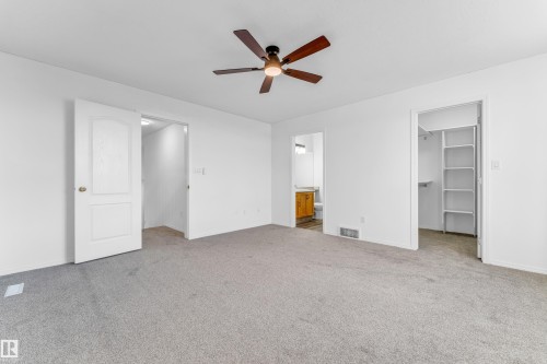 Carpeted room featuring a ceiling fan, white paneled door, and access to a bathroom with a wood-finish vanity and a closet with built-in shelving - 4103 37A Avenue, Edmonton, AB - Indoor Photo Showing Other Room