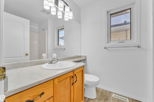 Bathroom featuring a light wood-finish vanity with an integrated sink, a neutral-toned countertop, a window with white trim, and wood-finish flooring - 4103 37A Avenue, Edmonton, AB - Indoor Photo Showing Bathroom