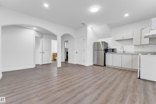 Open-concept living space featuring wood-finish flooring, recessed lighting, and a kitchen area with white cabinetry, stainless steel appliances, and a built-in range hood - 4103 37A Avenue, Edmonton, AB - Indoor Photo Showing Kitchen With Double Sink