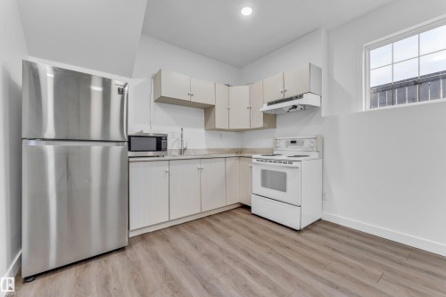 Compact kitchen featuring a stainless steel refrigerator, white electric range, and wood-finish flooring - 4103 37A Avenue, Edmonton, AB - Indoor Photo Showing Kitchen