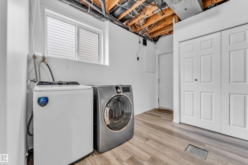 Dedicated laundry area featuring a window with horizontal blinds, wood-finish flooring, and white bifold closet doors - 4103 37A Avenue, Edmonton, AB - Indoor Photo Showing Laundry Room