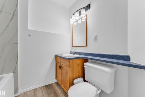 Bathroom featuring a wood-finish vanity with an integrated sink, a blue countertop, a framed mirror, and a five-light fixture - 4103 37A Avenue, Edmonton, AB - Indoor Photo Showing Bathroom