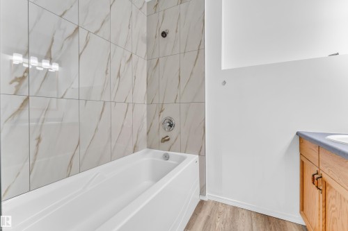 Bathtub with chrome fixtures and surround tiled in a white and gold veined pattern - 4103 37A Avenue, Edmonton, AB - Indoor Photo Showing Bathroom