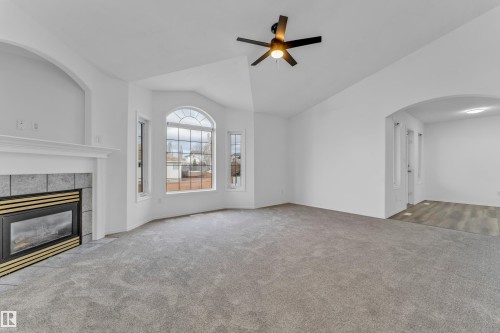 Living area featuring a fireplace with a tile surround and mantel, a bay window with an arched transom, a ceiling fan with integrated lighting, a vaulted ceiling, and an arched doorway - 4103 37A Avenue, Edmonton, AB - Indoor With Fireplace
