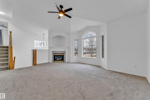 Spacious living area featuring a vaulted ceiling, a gas fireplace with a tiled surround and mantel, and a prominent bay window with an arched top - 4103 37A Avenue, Edmonton, AB - Indoor With Fireplace