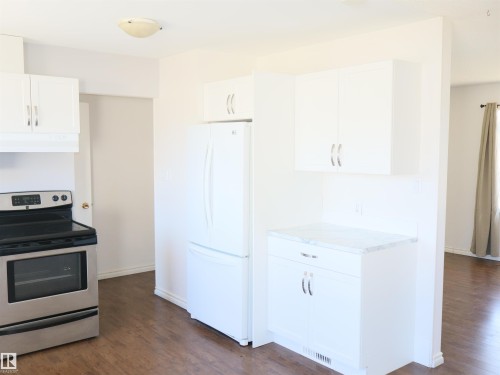 Kitchen featuring wood-finish flooring, white cabinetry with brushed nickel hardware, and a white refrigerator - 4934 49 Avenue, Barrhead, AB - Indoor Photo Showing Kitchen