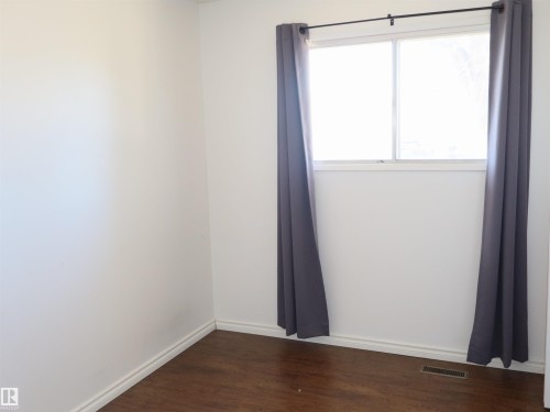 Bright interior space featuring a window with a dark curtain rod, white walls, white baseboards, and wood-finish flooring - 4934 49 Avenue, Barrhead, AB - Indoor Photo Showing Other Room