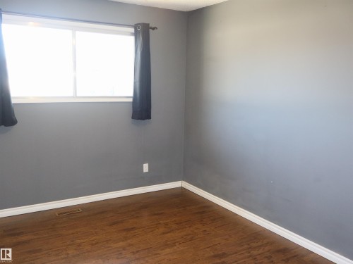 Spacious room featuring rich wood-finish flooring, white baseboards, and a large window - 4934 49 Avenue, Barrhead, AB - Indoor Photo Showing Other Room