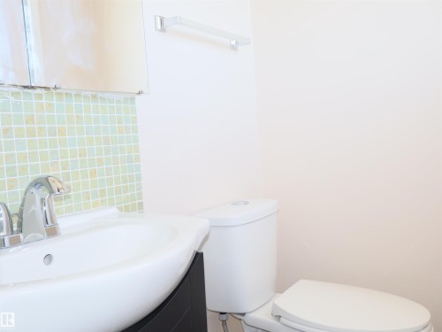 Bathroom featuring a white toilet, wall-mounted mirror, and a vanity with an integrated sink and chrome faucet - 4934 49 Avenue, Barrhead, AB - Indoor Photo Showing Bathroom