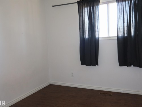 Bright interior space featuring a window with a curtain rod, wood-finish flooring, white baseboards, and a floor-level air vent - 4934 49 Avenue, Barrhead, AB - Indoor Photo Showing Other Room