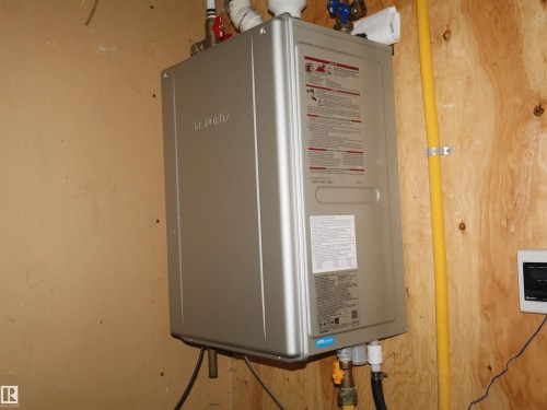 Wall-mounted water heating unit featuring visible plumbing and electrical connections - 4934 49 Avenue, Barrhead, AB - Indoor Photo Showing Basement
