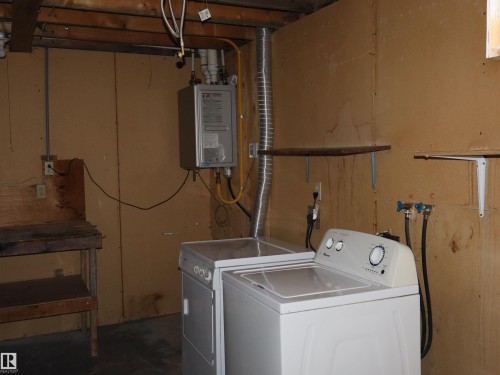 Utility space featuring a tankless water heater, exposed wood joists, and a built-in workbench - 4934 49 Avenue, Barrhead, AB - Indoor Photo Showing Laundry Room