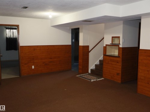 Finished lower level space featuring wood-finish paneling, a staircase with wood-finish handrail, and integrated wall shelving - 4934 49 Avenue, Barrhead, AB - Indoor Photo Showing Other Room
