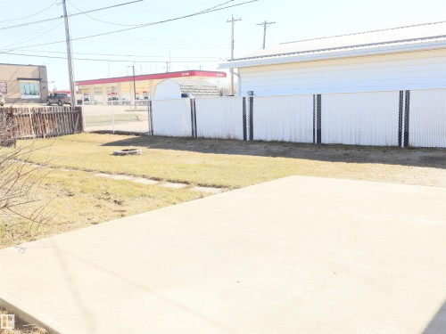 Concrete patio area bordered by a grassy expanse, featuring a chain-link fence with privacy slats - 4934 49 Avenue, Barrhead, AB - Outdoor