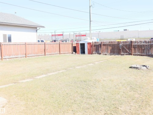 Spacious backyard featuring a full perimeter wood fence, a metal storage shed, and a circular stone fire pit - 4934 49 Avenue, Barrhead, AB - Outdoor
