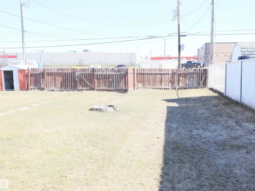 Expansive grass lawn featuring a red and white storage shed, a wood-panel fence, and a white chain-link fence - 4934 49 Avenue, Barrhead, AB - Outdoor