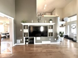 Living space featuring a built-in entertainment center with shelving, wood-finish flooring, and a high ceiling - 