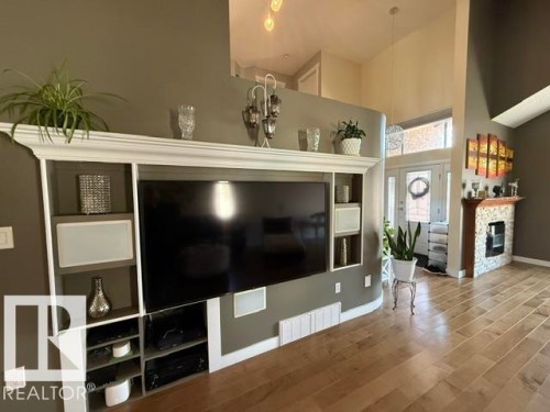 Custom built-in media center with integrated shelving and crown molding, wood-finish flooring, and a fireplace with a stone surround - 356 Weber Way, Edmonton, AB - Indoor Photo Showing Living Room With Fireplace