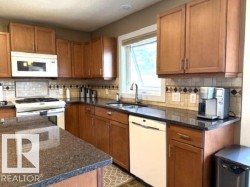 Kitchen featuring wood cabinetry, dark speckled countertops, white appliances, and a tiled backsplash with decorative accents - 