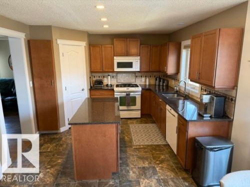 Kitchen featuring wood cabinetry, dark countertops, a central island, a white gas range, and a dual basin sink with a gooseneck faucet - 356 Weber Way, Edmonton, AB - Indoor Photo Showing Kitchen With Double Sink