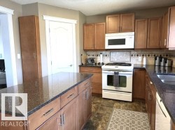 Kitchen featuring a central island with a speckled dark countertop, wood-finish cabinetry, stainless-steel hardware, an integrated sink, and an over-range microwave - 