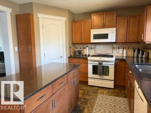 Kitchen featuring wood cabinetry, dark granite countertops, stainless steel sink, tile flooring, and a patterned tile backsplash - 356 Weber Way, Edmonton, AB - Indoor Photo Showing Kitchen