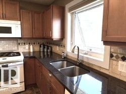 Kitchen featuring a double stainless steel sink, dark stone-finish countertops, wood-finish cabinetry, a tiled backsplash with decorative accents, and an overhead microwave - 