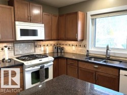 Kitchen featuring wood cabinetry, dark countertops, and a tile backsplash with decorative accents - 