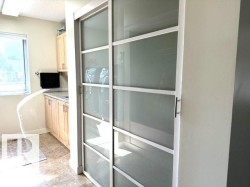 Modern sliding frosted glass doors paired with a utility area featuring light wood cabinetry, a light-colored countertop, and a window - 