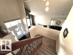 Multi-level interior featuring a carpeted staircase with wood railings, a two-story foyer with transom windows, a decorative chandelier, and an open concept living area - 