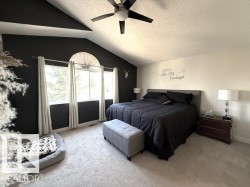 Spacious bedroom featuring vaulted ceilings, a ceiling fan, and three windows including an arched transom - 