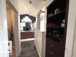 Hallway featuring a built-in dark wood shelving unit with drawers and a view into a bathroom with a vaulted ceiling and dual vanity - 