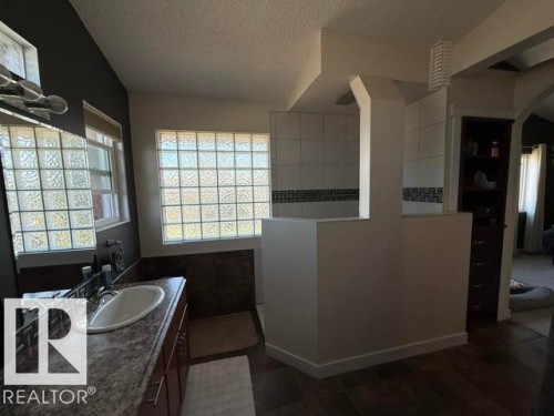 Bathroom featuring glass block windows, a single vanity with an oval basin, wood-finish flooring, a walk-in shower with tile surround, and a dark wood built-in cabinet - 356 Weber Way, Edmonton, AB - Indoor Photo Showing Bathroom
