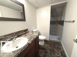 Bathroom featuring a dark wood-finish vanity with a white oval sink, a patterned countertop, and a mosaic tile backsplash - 