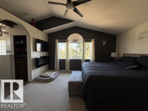 Vaulted ceiling with a ceiling fan, arched doorway, built-in shelving, mounted fireplace, and large windows with exterior views - 356 Weber Way, Edmonton, AB - Indoor Photo Showing Bedroom