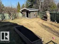 Spacious backyard featuring a storage shed with siding, a stone outdoor fireplace, a raised wooden garden bed, and a wooden privacy fence - 