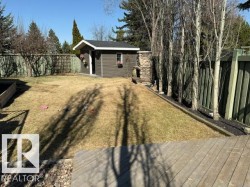 Spacious backyard featuring a storage shed with white trim, a wood deck, a raised garden bed, and mature trees lining the perimeter - 