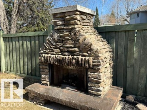 Stone outdoor fireplace with a solid stone hearth, surrounded by a wood privacy fence - 356 Weber Way, Edmonton, AB - Outdoor
