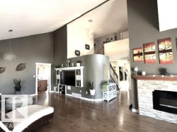 Living area featuring vaulted ceilings, wood-finish flooring, a built-in media center, a stone-clad fireplace, and a staircase with an open railing - 