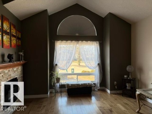 Spacious interior featuring vaulted ceilings with an arched transom window, a stone-clad fireplace, and wood-finish flooring - 356 Weber Way, Edmonton, AB - Indoor