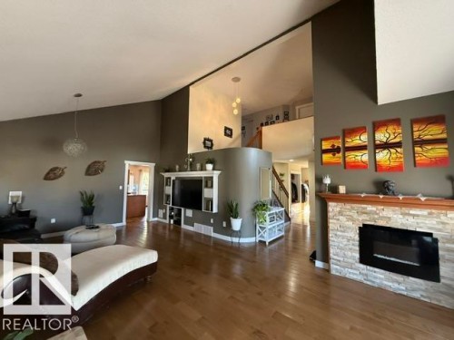 Spacious living area featuring wood-finish flooring, a stone-clad fireplace, and a built-in media center - 356 Weber Way, Edmonton, AB - Indoor Photo Showing Living Room With Fireplace