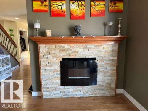 Modern fireplace featuring a stacked stone surround, a wood mantel, and a black-framed insert - 356 Weber Way, Edmonton, AB - Indoor With Fireplace
