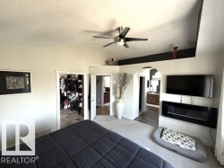 Carpeted room featuring a ceiling fan with integrated lighting, a wall-mounted electric fireplace, and an arched doorway leading to a tiled room with a double vanity - 