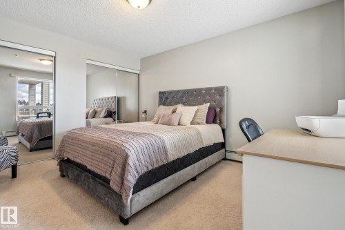 Carpeted room featuring mirrored sliding closet doors, a neutral wall color, and a built-in light-tone desk - 1306 330 Clareview Station Drive, Edmonton, AB - Indoor Photo Showing Bedroom