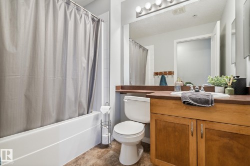 Bathroom featuring a white bathtub, wood-finish vanity with an integrated sink, broad wall mirror, and tile flooring - 1306 330 Clareview Station Drive, Edmonton, AB - Indoor Photo Showing Bathroom