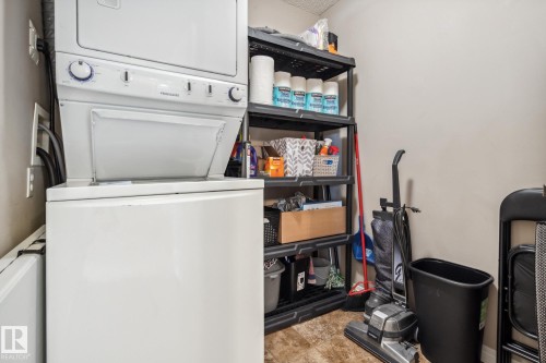 Dedicated utility space featuring a stacked washer and dryer unit, durable vinyl flooring, and a multi-tiered shelving unit for organized storage - 1306 330 Clareview Station Drive, Edmonton, AB - Indoor Photo Showing Laundry Room