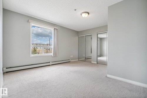 Spacious room featuring light gray walls, plush carpeting, a large window, two mirrored sliding closet doors, and baseboard heating - 1306 330 Clareview Station Drive, Edmonton, AB - Indoor Photo Showing Other Room