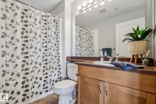 Bathroom featuring a wood-finish vanity with a built-in sink, a large mirror with vanity lighting, and a bathtub with a shower - 1306 330 Clareview Station Drive, Edmonton, AB - Indoor Photo Showing Bathroom