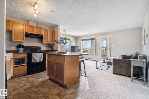 Open-concept kitchen featuring wood cabinetry, black appliances, a central island, and patterned flooring - 1306 330 Clareview Station Drive, Edmonton, AB - Indoor Photo Showing Kitchen
