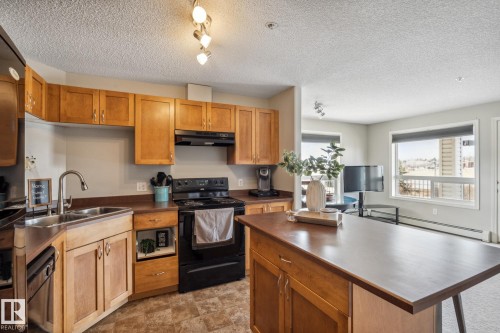 Functional kitchen featuring wood cabinetry, a double basin stainless steel sink with a gooseneck faucet, black appliances, and durable countertop surfaces - 1306 330 Clareview Station Drive, Edmonton, AB - Indoor Photo Showing Kitchen With Double Sink